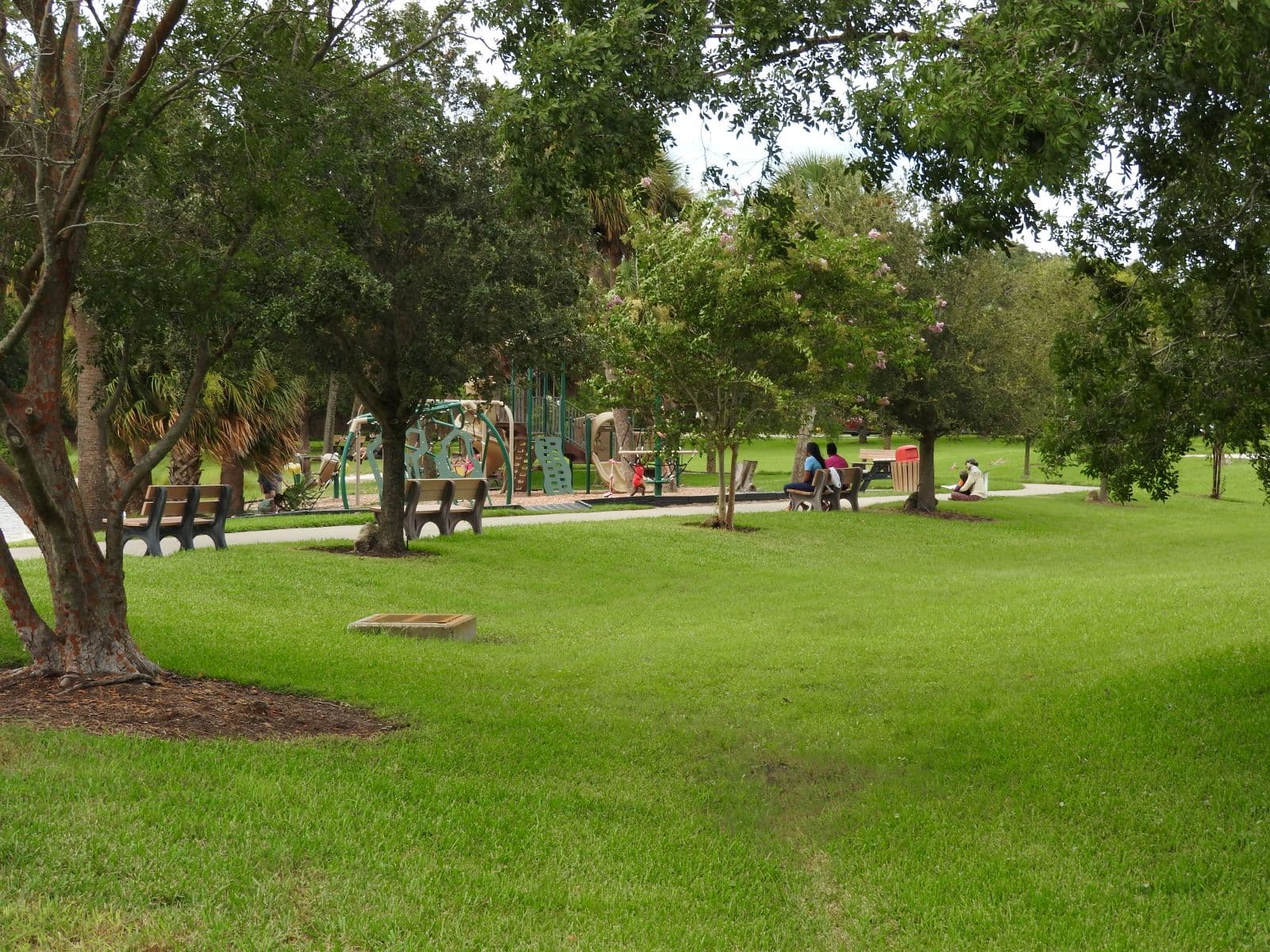 Playground, benches, and paved paths beneath mature trees at Fortunato Park.