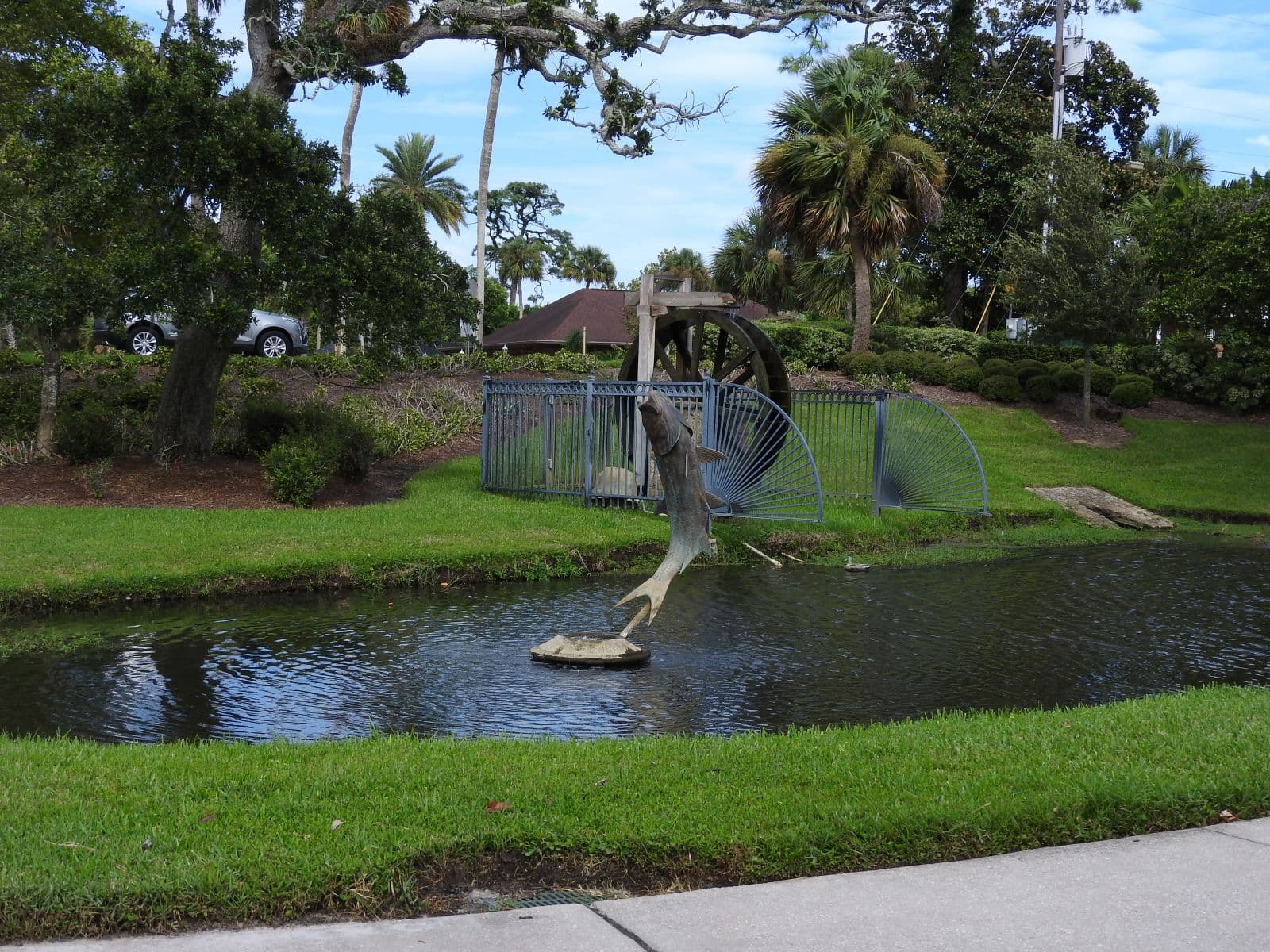 Fish sculpture and water wheel beside a landscaped pond at Rockefeller Gardens.